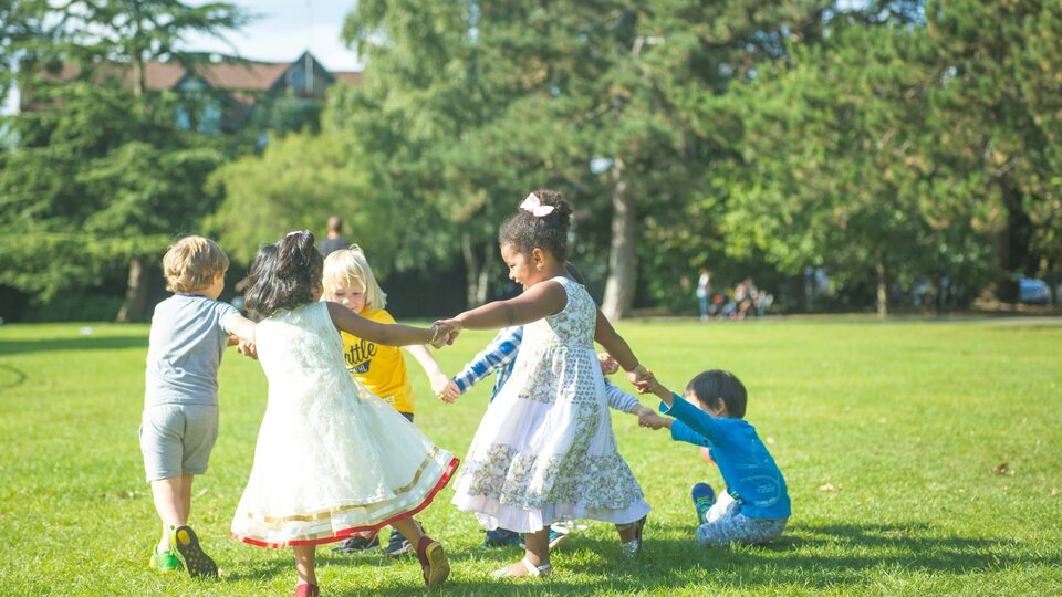 Six children outside, holding hands to form a circle.