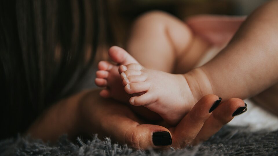 The feet of an infant resting in the hand of an adult.